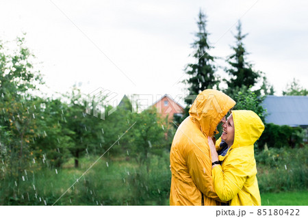 A married couple in yellow raincoats in the rain in their backyard. Front view. A married couple in yellow raincoats in the rain in their backyard. Front view. 85180422