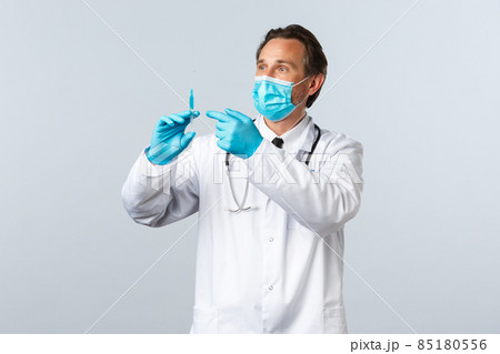 Covid-19, preventing virus, healthcare workers and vaccination concept. Middle-aged doctor in medical mask and gloves holding syringe with coronavirus vaccine or hiv prep, prepare shot for patient 85180556