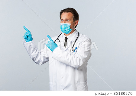 Covid-19, preventing virus, healthcare workers and vaccination concept. Upset gloomy doctor in medical mask receive bad results, frowning pointing upper left corner, distressed over awful news Covid-19, preventing virus, healthcare workers and vaccination concept. Upset gloomy doctor in medical mask receive bad results, frowning pointing upper left corner, distressed over awful news 85180576