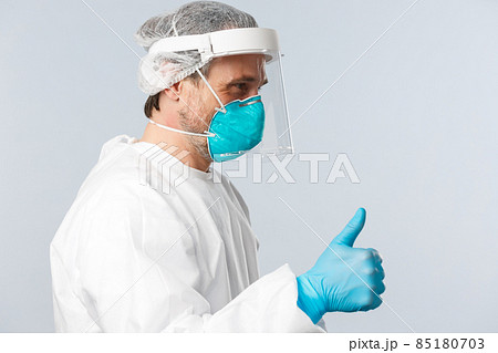 Covid-19, preventing virus, healthcare workers and vaccination concept. Profile of cheerful doctor in personal protective equipment showing thumb-up patient, ensure all good, nothing worry about Covid-19, preventing virus, healthcare workers and vaccination concept. Profile of cheerful doctor in personal protective equipment showing thumb-up patient, ensure all good, nothing worry about 85180703