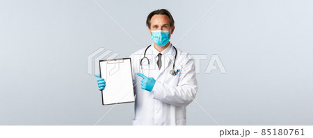 Covid-19, preventing virus, healthcare workers and vaccination concept. Professional doctor at clinic pointing at clipboard paper, explain disease or showing chart, wear medical mask and gloves 85180761