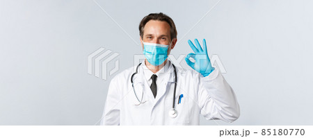 Covid-19, preventing virus, healthcare and vaccination concept. Happy smiling doctor in medical mask and gloves assure all good, show okay sign as guarantee safety and quality of service in clinic 85180770
