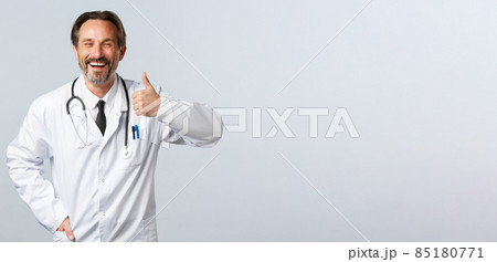 Covid-19, coronavirus outbreak, healthcare workers and pandemic concept. Optimistic happy doctor advice medication or clinic service, ensure quality, showing thumbs-up in approval 85180771