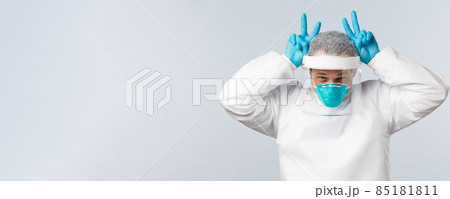 Covid-19, preventing virus, healthcare workers and vaccination concept. Happy optimistic doctor in personal protective equipment showing bunny ears gesture with fingers up above head 85181811