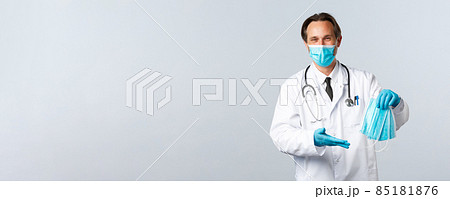 Covid-19, preventing virus, healthcare workers and vaccination concept. Cheerful doctor in clinic wearing PPE received medical masks for hospital employees, standing white background 85181876