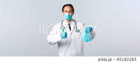 Covid-19, preventing virus, healthcare workers and vaccination concept. Satisfied doctor in medical mask and gloves recommend PPE, show thumb-up as guarantee quality of masks 85182263