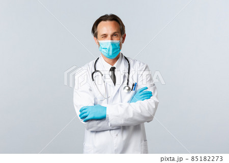 Covid-19, preventing virus, healthcare workers and vaccination concept. Friendly professional doctor in medical mask and gloves, encourage patient relax, all good, winking and cross arms chest Covid-19, preventing virus, healthcare workers and vaccination concept. Friendly professional doctor in medical mask and gloves, encourage patient relax, all good, winking and cross arms chest 85182273