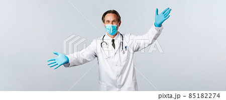 Covid-19, preventing virus, healthcare workers and vaccination concept. Friendly doctor in medical mask and gloves spread hands welcoming, greeting clinic patients, inviting come in Covid-19, preventing virus, healthcare workers and vaccination concept. Friendly doctor in medical mask and gloves spread hands welcoming, greeting clinic patients, inviting come in 85182274