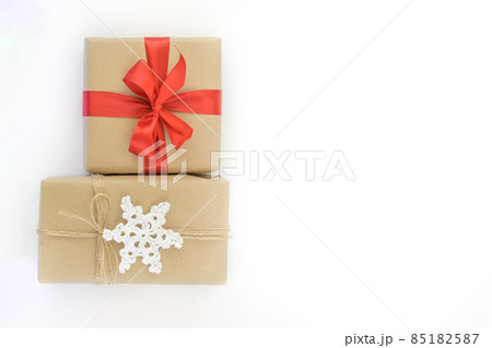 Christmas and New Years flatlay background. Gift box wrapped in kraft paper with jute cord. Decorated with a crocheted snowflake. Box with a red ribbon. Place for your text 85182587