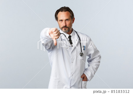 Covid-19, coronavirus outbreak, healthcare workers and pandemic concept. Disappointed serious male doctor in white coat, frowning displeased and show thumb-down, disapprove action 85183312