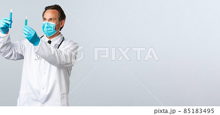 Covid-19, preventing virus, healthcare workers and vaccination concept. Professional clinic lab doctor in medical mask and gloves compare two test-tubes with vaccines, white background 85183495