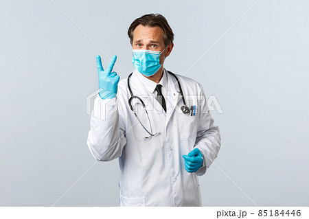 Covid-19, preventing virus, healthcare workers and vaccination concept. Serious concerned doctor in medical mask and gloves show number two, twice as prescribe medication, white background Covid-19, preventing virus, healthcare workers and vaccination concept. Serious concerned doctor in medical mask and gloves show number two, twice as prescribe medication, white background 85184446