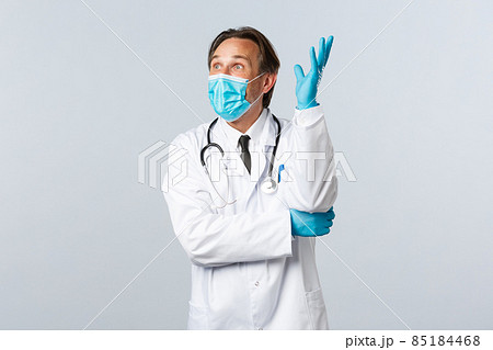 Covid-19, preventing virus, healthcare workers and vaccination concept. Excited upbeat male doctor in medical mask and gloves, raising hand up thoughtful, have idea, look amazed 85184468