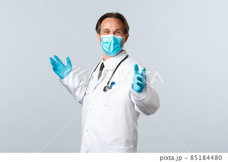 Covid-19, preventing virus, healthcare workers and vaccination concept. Cheerful glad doctor in medical mask and gloves, spread hands sideways relieved, celebrating good news, white background 85184480