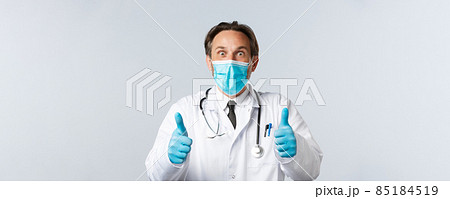 Covid-19, preventing virus, healthcare workers and vaccination concept. Excited and surprised happy doctor in medical mask and gloves, showing thumbs-up thrilled, hear great news, agree and approve Covid-19, preventing virus, healthcare workers and vaccination concept. Excited and surprised happy doctor in medical mask and gloves, showing thumbs-up thrilled, hear great news, agree and approve 85184519