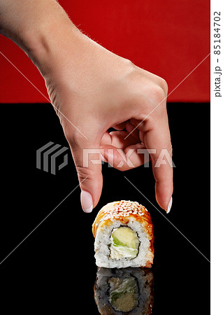 Female hand reaching out to unagi roll with eel, cream cheese and avocado Female hand reaching out to unagi roll with eel, cream cheese and avocado 85184702