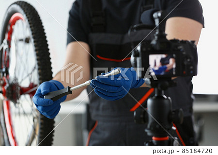 Blogger mechanic fix bicycle in workshop, busy young worker in shirt and gloves 85184720