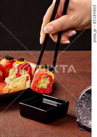 Female hand holding red rice sushi roll with tuna with chopsticks over soy sauce Female hand holding red rice sushi roll with tuna with chopsticks over soy sauce 85184803