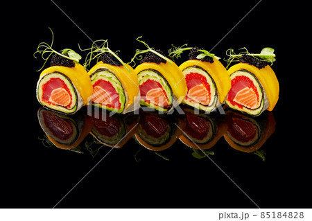 No-rice sushi roll with tuna, salmon, tobiko, avocado in mamenori topped with mango, caviar on black background No-rice sushi roll with tuna, salmon, tobiko, avocado in mamenori topped with mango, caviar on black background 85184828