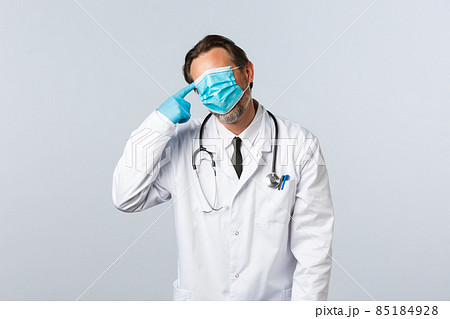 Covid-19, preventing virus, healthcare workers and vaccination concept. Tired and distressed doctor fighting coronavirus, exhausted work, pull mask on whole face and make shot gun gesture near head 85184928