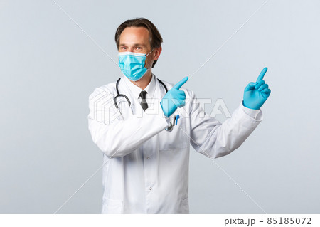 Covid-19, preventing virus, healthcare workers and vaccination concept. Charismatic pleased doctor give advice, wear medical mask and gloves pointing upper right corner at advertisement Covid-19, preventing virus, healthcare workers and vaccination concept. Charismatic pleased doctor give advice, wear medical mask and gloves pointing upper right corner at advertisement 85185072