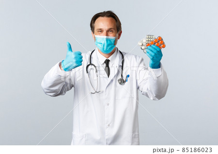 Covid-19, preventing virus, healthcare workers and vaccination concept. Satisfied handsome doctor smiling, wear medical mask and gloves, thumb-up as recommend pills, show good medication Covid-19, preventing virus, healthcare workers and vaccination concept. Satisfied handsome doctor smiling, wear medical mask and gloves, thumb-up as recommend pills, show good medication 85186023