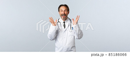 Covid-19, coronavirus outbreak, healthcare workers and pandemic concept. Excited happy male doctor telling great news, raising hands up and smiling thrilled, reacting to awesome promo 85186066