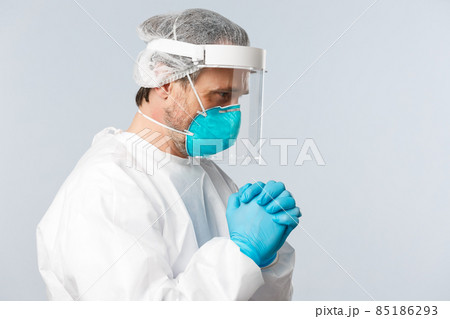 Covid-19, preventing virus, healthcare workers and vaccination concept. Profile of hopeful doctor in personal protective equipment, praying god, pleading or supplicating at hospital 85186293