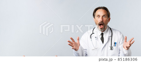 Covid-19, preventing virus, healthcare workers and vaccination concept. Shocked and concerned doctor in white coat drop jaw, gasping startled hear bad news, raising hands in dismay 85186306