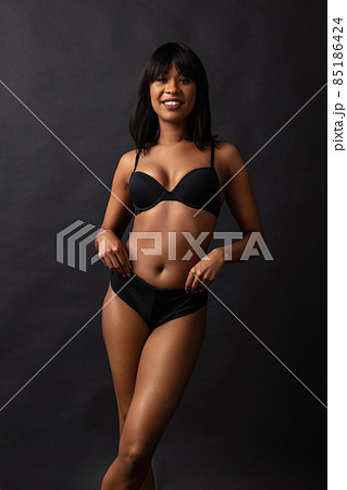 Full-length portrait of young beautiful slim girl in black underwear posing isolated over dark studio background. Natural beauty concept. 85186424