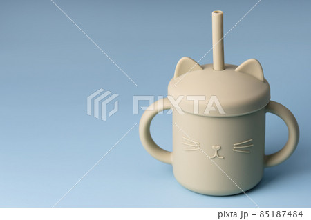 Green sippy cup on blue background. Silicone baby dishes, first soft cup for toddler. Baby tableware. Nutrition and feeding concept. Free space for text Green sippy cup on blue background. Silicone baby dishes, first soft cup for toddler. Baby tableware. Nutrition and feeding concept. Free space for text 85187484