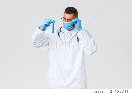 Covid-19, healthcare workers, pandemic and preventing virus concept. Thoughtful and intrigued doctor in medical mask and gloves, look interested at test-tube with new coronavirus vaccine 85187731