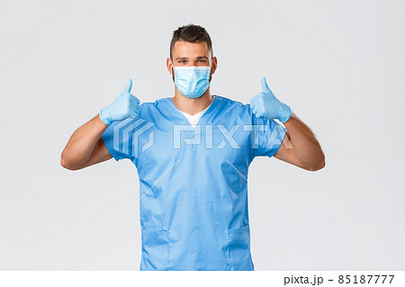 Healthcare workers, covid-19, coronavirus and preventing virus concept. Optimistic supportive male doctor, nurse in medical mask and scrubs, show thumbs-up in approval or recommendation Healthcare workers, covid-19, coronavirus and preventing virus concept. Optimistic supportive male doctor, nurse in medical mask and scrubs, show thumbs-up in approval or recommendation 85187777