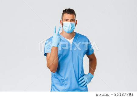 Healthcare workers, covid-19, coronavirus and preventing virus concept. Serious handsome doctor, nurse in blue scrubs and medical mask, showing number two or victory, look confident 85187793