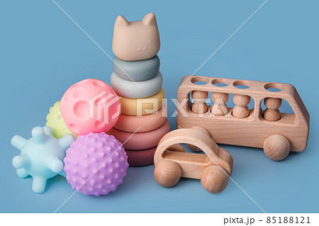 Colorful educational montessori kids toys on a blue background. Sensory balls for kids, wooden cars and silicone pyramid, textured plastic multi ball set for babies and toddlers, tower toy 85188121