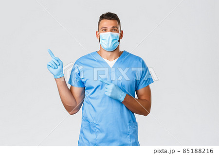 Healthcare workers, covid-19, coronavirus and preventing virus concept. Happy professional male nurse, doctor in scrubs and medical mask, gloves pointing finger left, showing banner Healthcare workers, covid-19, coronavirus and preventing virus concept. Happy professional male nurse, doctor in scrubs and medical mask, gloves pointing finger left, showing banner 85188216