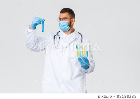 Covid-19, healthcare workers, pandemic and preventing virus concept. Talented doctor or lab clinic employee in white scrubs and medical mask, look at test-tube, researching samples, work on vaccine Covid-19, healthcare workers, pandemic and preventing virus concept. Talented doctor or lab clinic employee in white scrubs and medical mask, look at test-tube, researching samples, work on vaccine 85188235