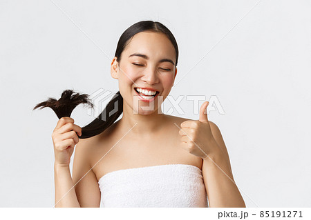 Beauty, hair loss products, shampoo and hair care concept. Close-up of satisfied, happy asian girl in bath towel showing thumbs-up and healthy hair ends, standing pleased white background 85191271