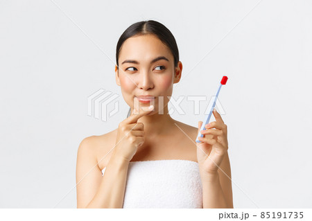 Beauty, personal care, and hygiene concept. Close-up of thoughtful and cunning attractive asian woman in bath towel, holding toothbrush and thinking, have idea while brush teeth, white background Beauty, personal care, and hygiene concept. Close-up of thoughtful and cunning attractive asian woman in bath towel, holding toothbrush and thinking, have idea while brush teeth, white background 85191735