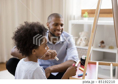 Happy cute Black little kid and dad drawing on chalkboard Happy cute Black little kid and dad drawing on chalkboard 85192210