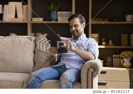 Happy man holding digital device, resting on couch at home Happy man holding digital device, resting on couch at home 85192217