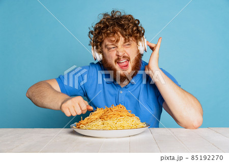 Emotional young hairy red-bearded man tasting large portion of noodles, pasta isolated on blue studio background. Emotional young hairy red-bearded man tasting large portion of noodles, pasta isolated on blue studio background. 85192270