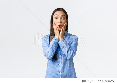 Surprised and astounded beautiful asian girl react to wonderful unexpected news, looking amazed with hands over face and opened mouth, standing in pajamas over white background 85192625