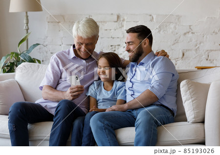 Happy three male generations family using cellphone apps at home. 85193026