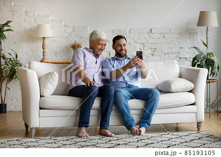 Happy young man using cellphone with older father. Happy young man using cellphone with older father. 85193105