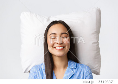 Smiling dreamy and beautiful asian female lying in bed on pillow, wearing blue pajamas, close eyes and grinning, daydreaming or sleeping at night, imaging something cute, white background Smiling dreamy and beautiful asian female lying in bed on pillow, wearing blue pajamas, close eyes and grinning, daydreaming or sleeping at night, imaging something cute, white background 85193371