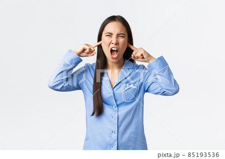 Angry and pissed-off young asian woman in blue pajamas screaming with ears shut, plug fingers from disturbing loud noise at night, complaining neighbour music, cant sleep, standing white background Angry and pissed-off young asian woman in blue pajamas screaming with ears shut, plug fingers from disturbing loud noise at night, complaining neighbour music, cant sleep, standing white background 85193536