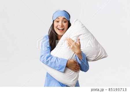 Smiling excited pretty asian girl in blue pajamas and sleeping mask, hugging soft comfortable pillow and looking surprised or amazed at camera at sleepover, white background Smiling excited pretty asian girl in blue pajamas and sleeping mask, hugging soft comfortable pillow and looking surprised or amazed at camera at sleepover, white background 85193713