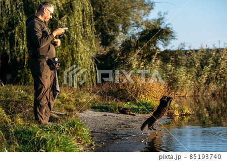 Homeless hungry black cat catching fish with fisherman on the river bank. Stray hungry black cat gets food Homeless hungry black cat catching fish with fisherman on the river bank. Stray hungry black cat gets food 85193740