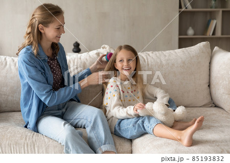 Happy young mother detangling hair of little daughter. Happy young mother detangling hair of little daughter. 85193832